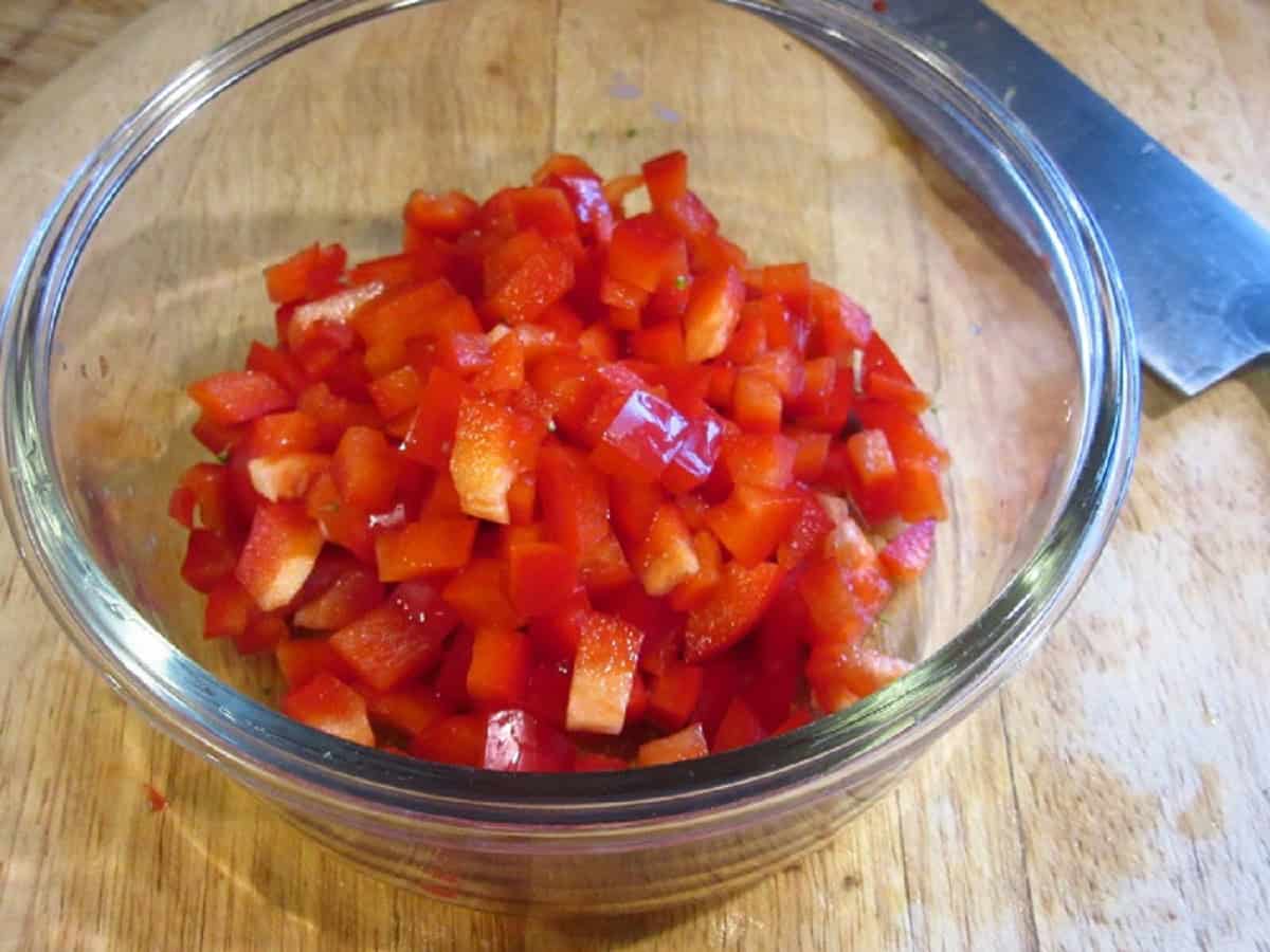Chopped red peppers in a clear bowl and a knife.
