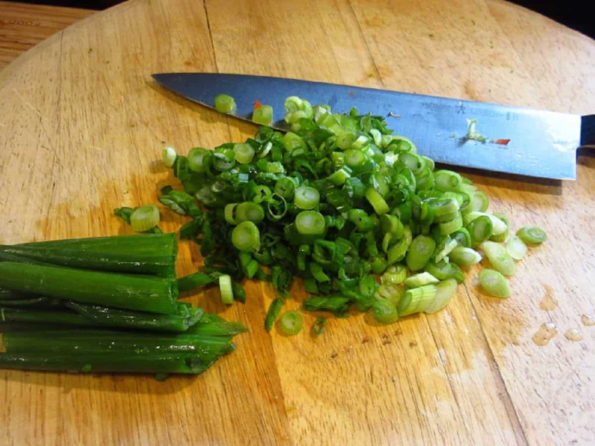 Chopped scallions on a wooden cutting board and knife.