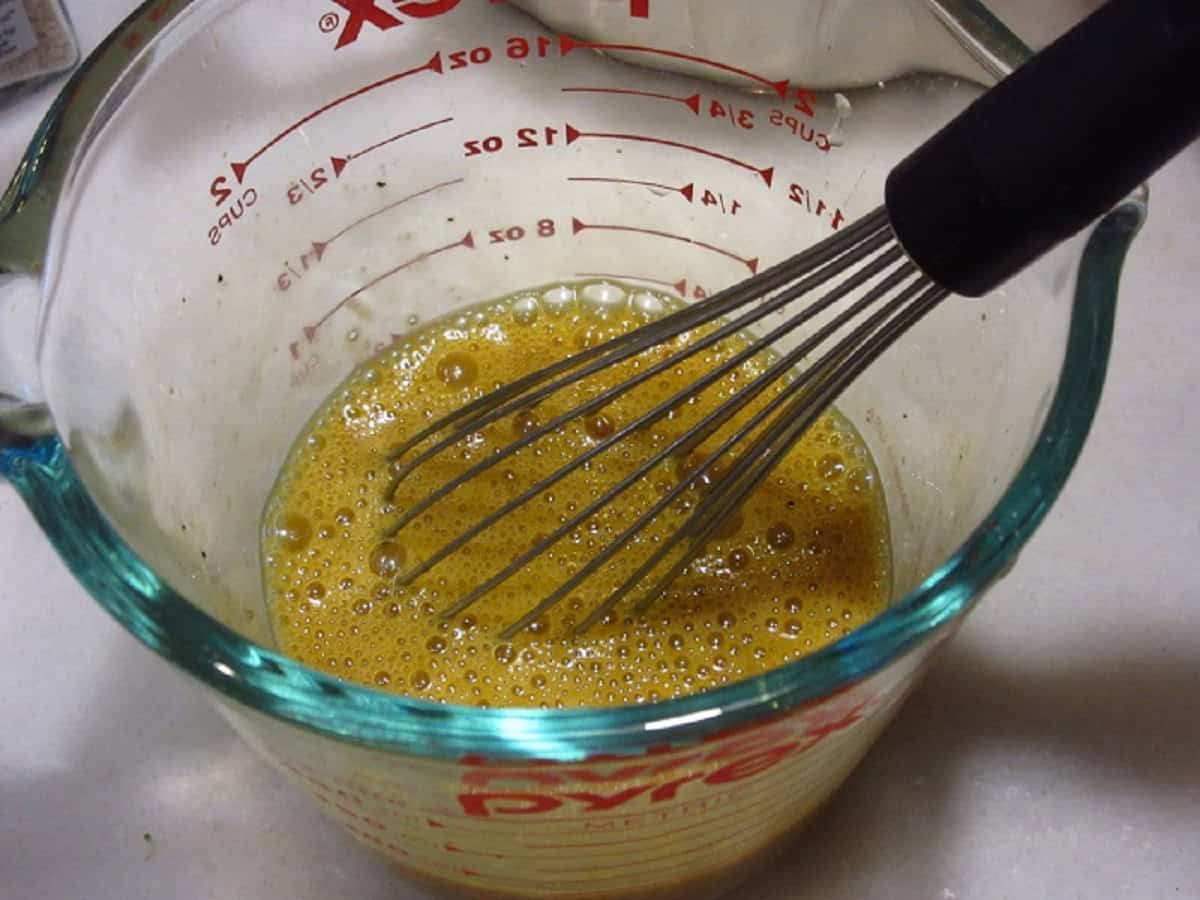 Glass measuring cup with whipped eggs and a whisk.