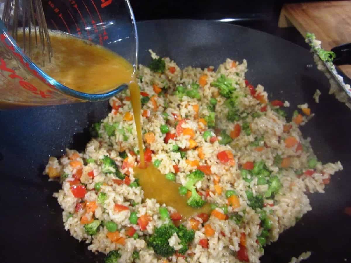 Sauce being poured onto stir-fried brown rice in a wok.