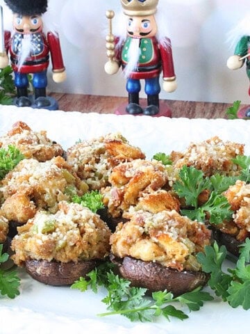 Stuffed cremini mushroom caps on a white platter surrounded by pasrley.