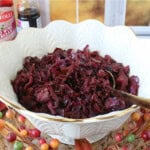 A golden serving spoon in a large white bowl filled with Sweet and Sour Red Cabbage.