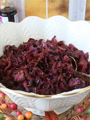 A golden serving spoon in a large white bowl filled with Sweet and Sour Red Cabbage.