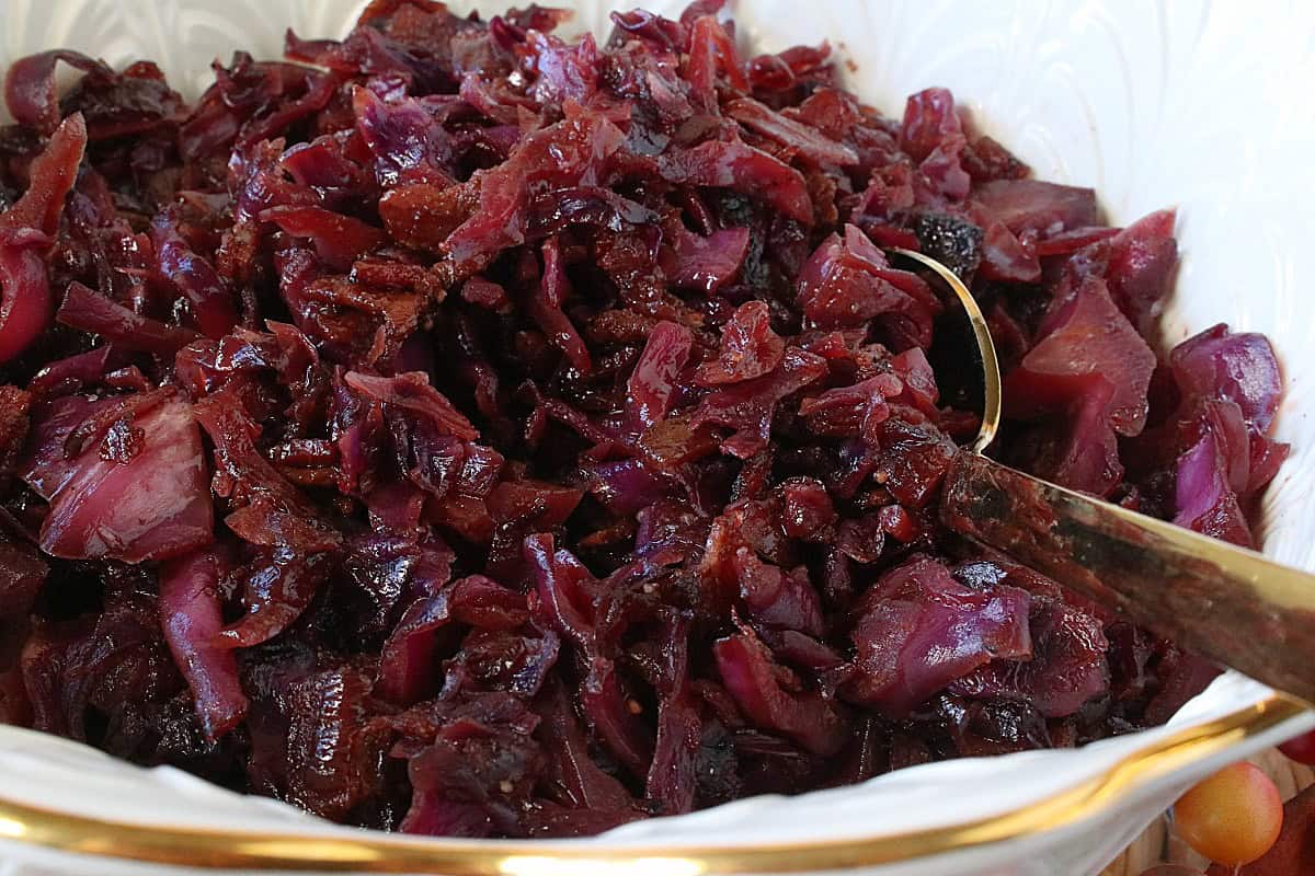 A serving spoon in a pretty bowl filled with ruby red Sweet and Sour Red Cabbage with Bacon.