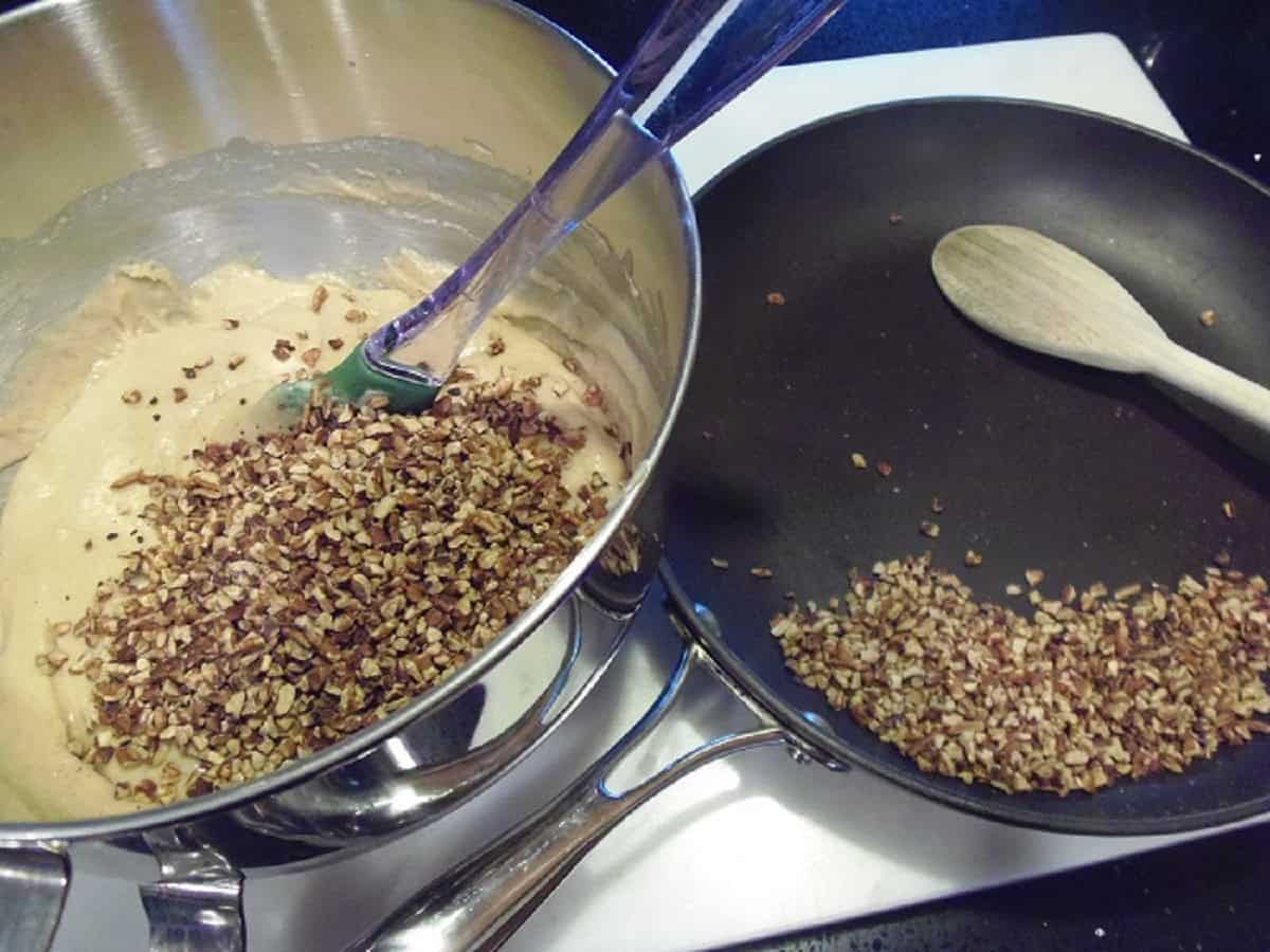 Toasted pecans being divided into a cupcake batter and in a skillet.