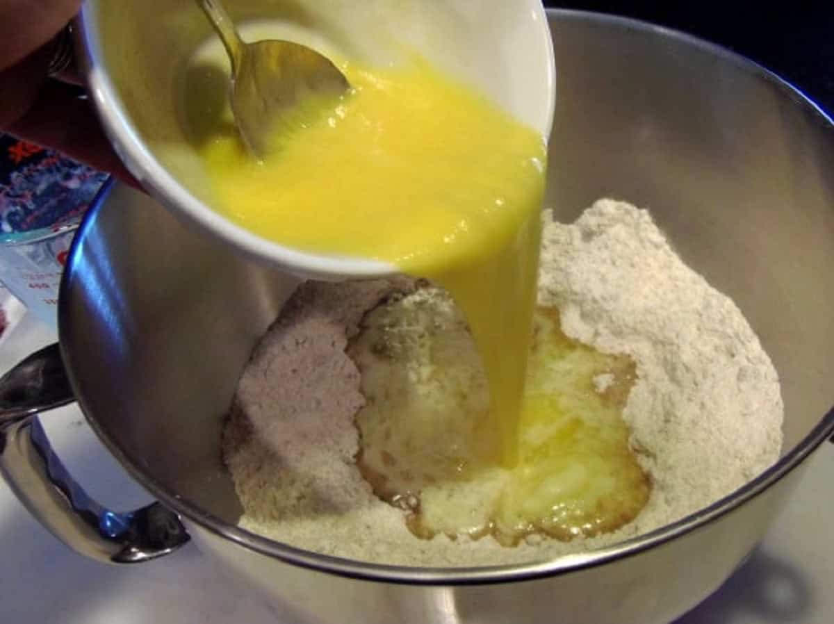 Beaten eggs and butter being added to a bowl with dry ingredients.