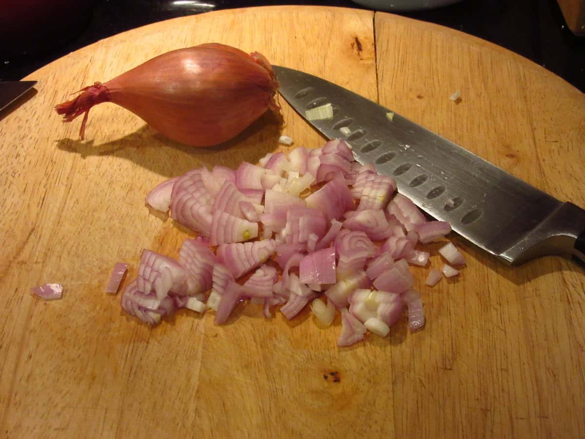 Chopped shallots on a wooden cutting board.
