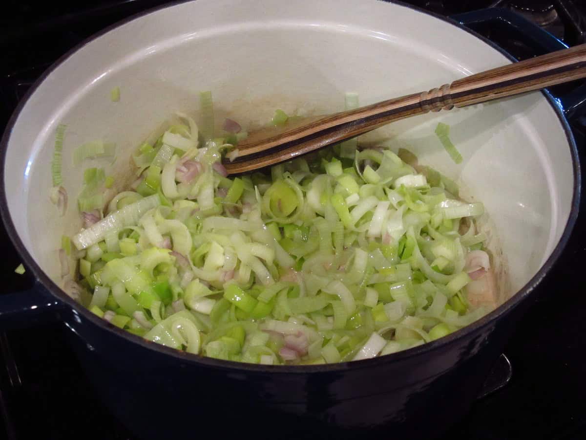 A wooden spoon in a pot of leeks and shallots cooking on the stovetop.
