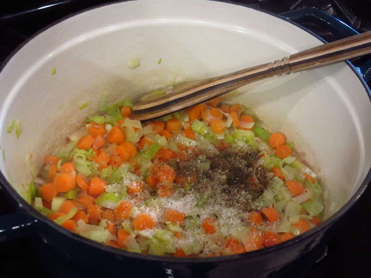 Salt and pepper in a pot of carrots, leeks and shallots to make soup.