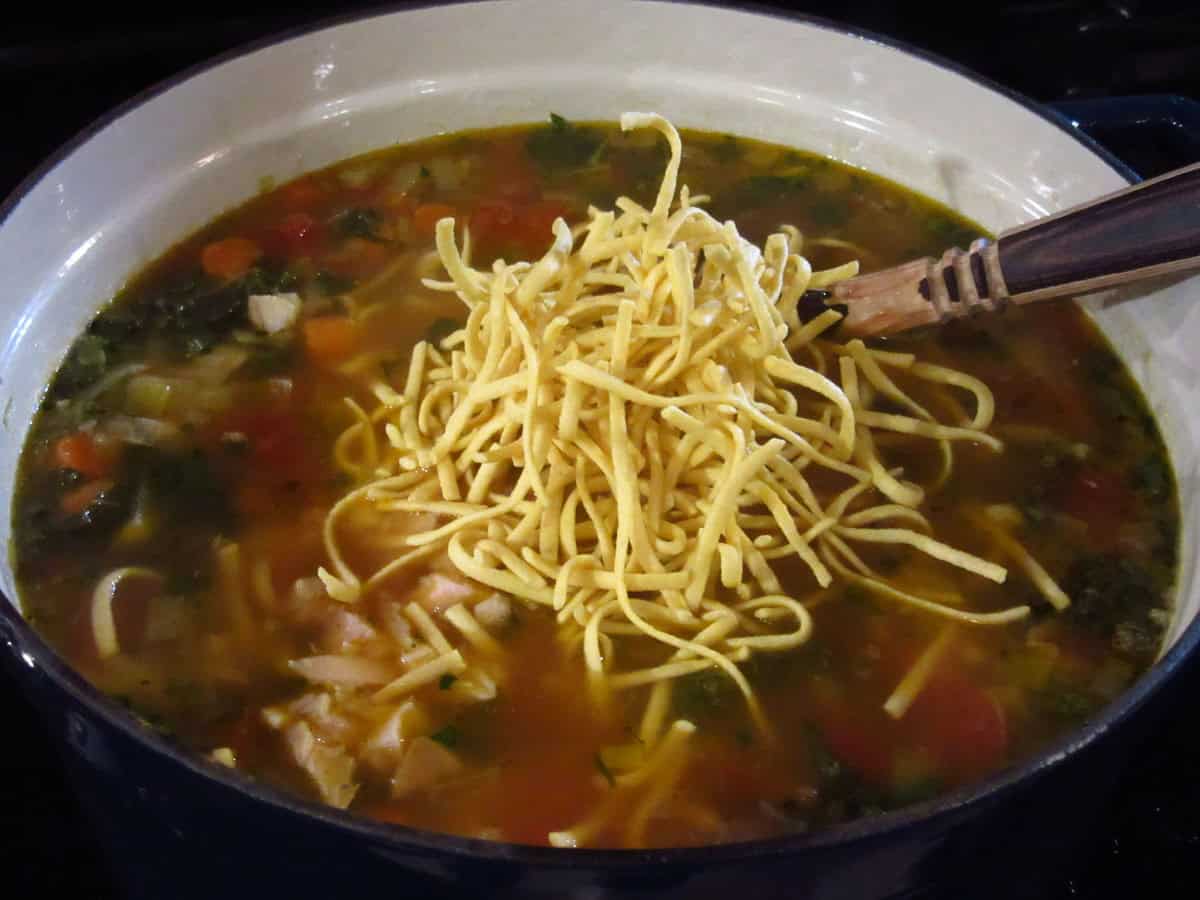 Dry noodles being added to a pot of soup.