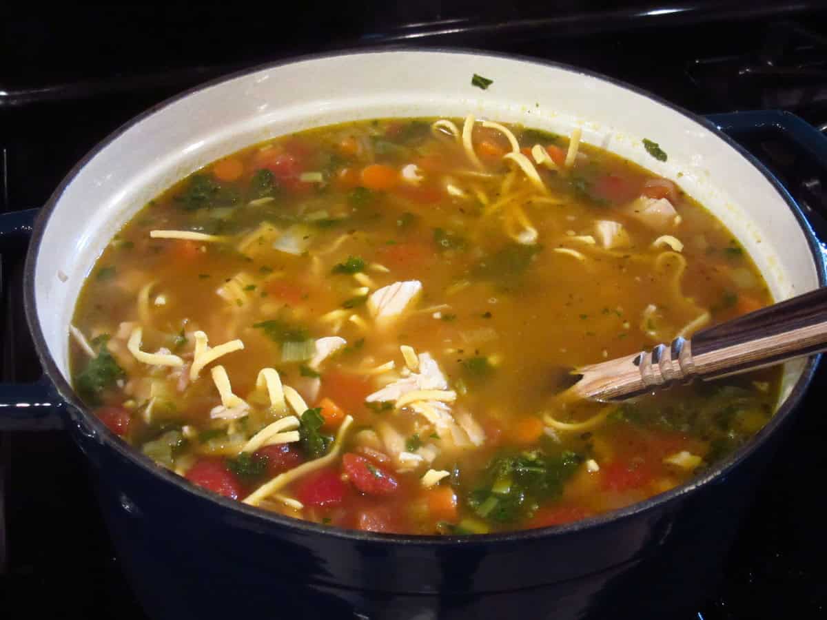 An inviting looking pot of Chicken Noodle Soup with kale and leeks on the stovetop.