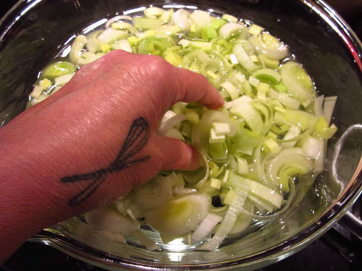 A hand separating slices of leek in a bowl of water.
