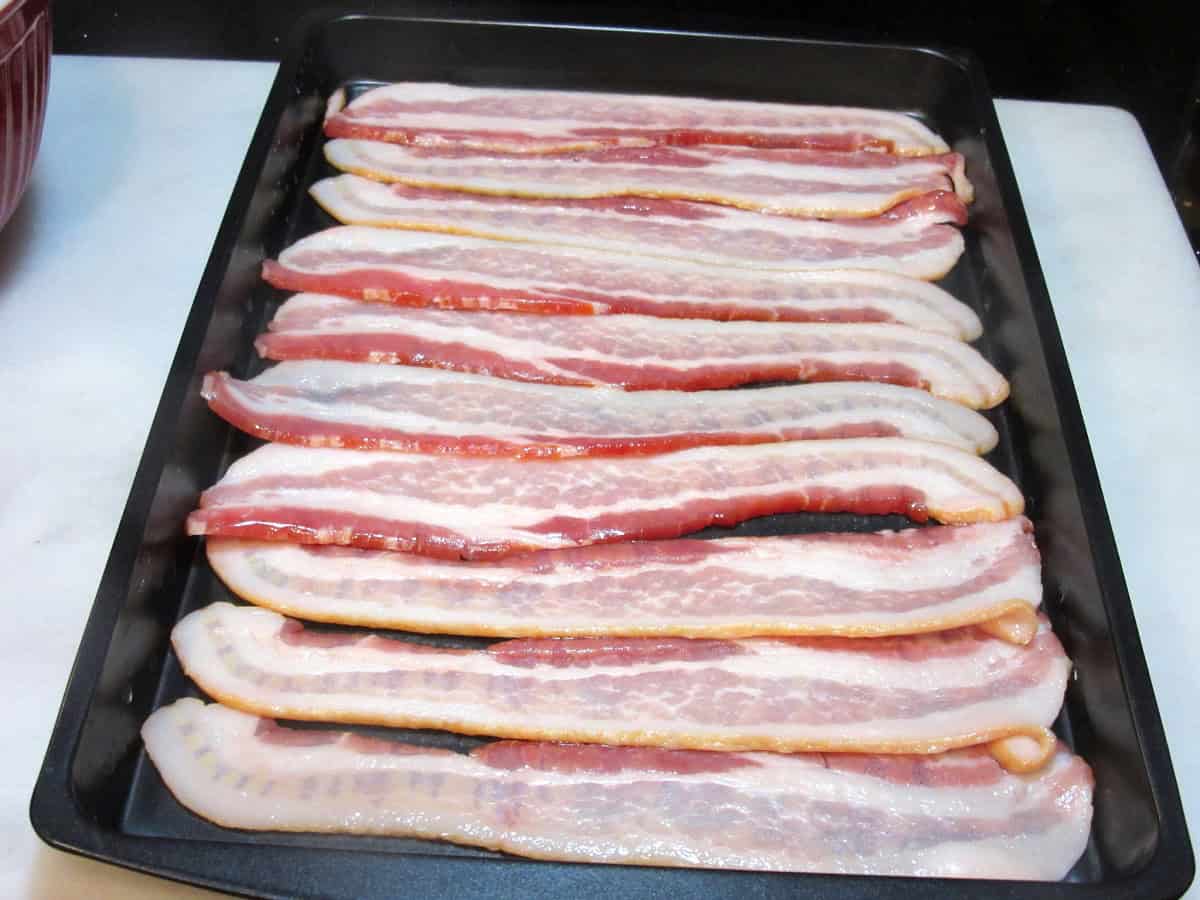 Uncooked strips of bacon laid out on a baking sheet.