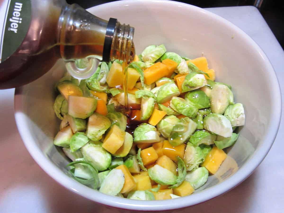 Maple syrup being drizzled onto Brussels sprouts and butternut squash in a bowl.