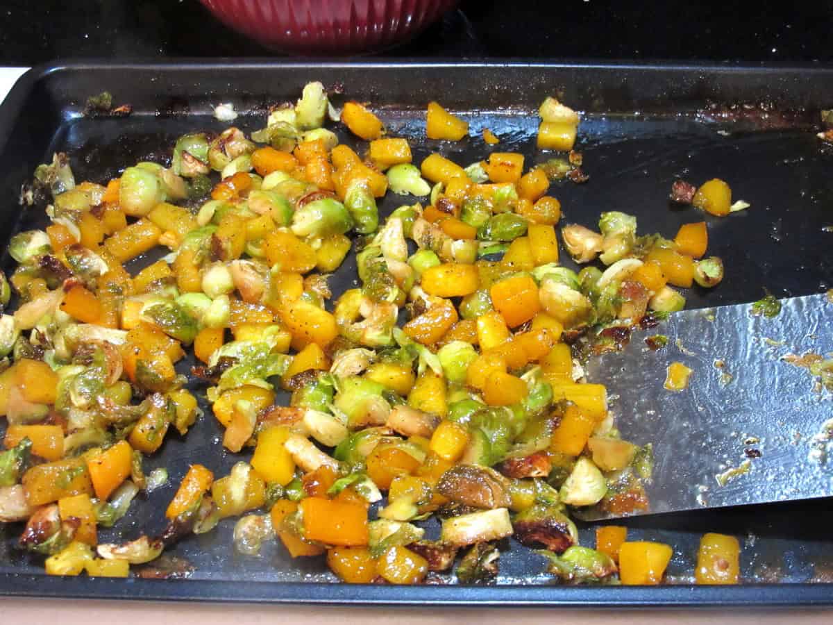 Roasted butternut squash and Brussels sprouts on a baking sheet with a spatula.