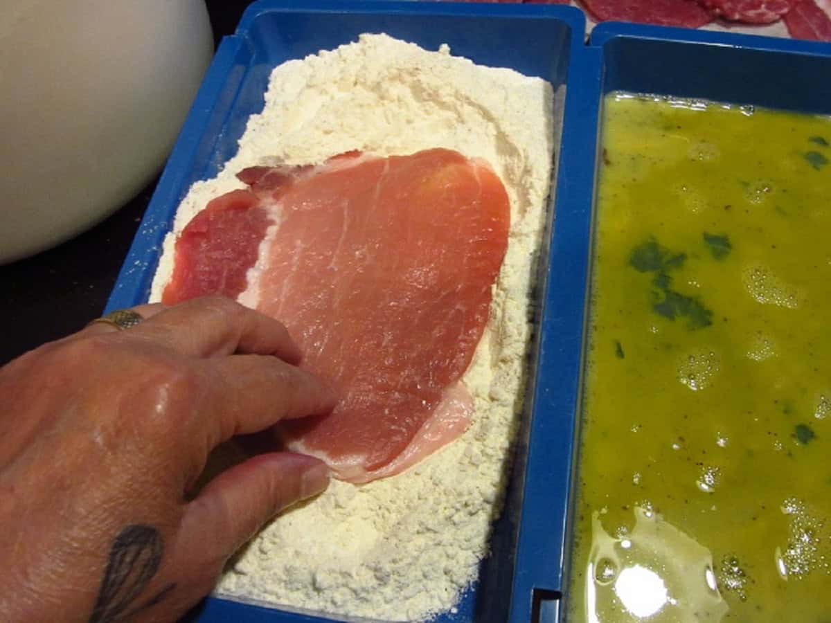 A thin pork cutlet being dipped in flour.