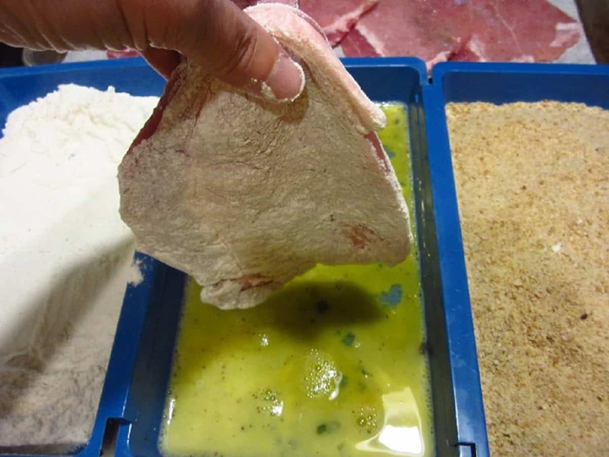 A pork cutlet being dredged in flour.