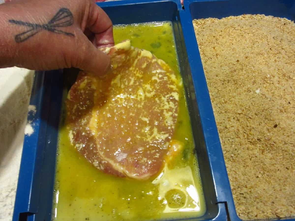 A pork cutlet being dipped in egg wash.