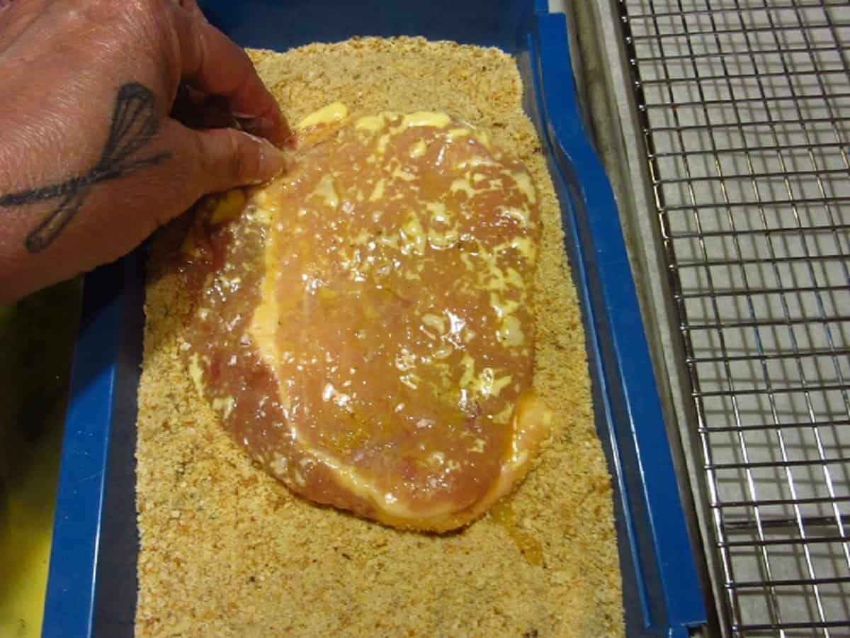 A pork cutlet being dredged in breadcrumbs.