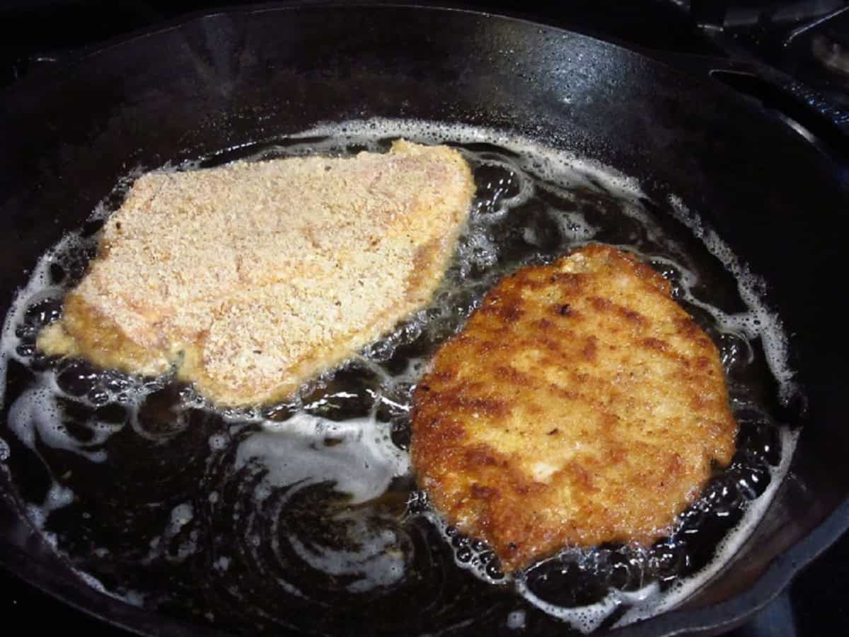 Two pork schnitzel in a cast iron skillet with oil.