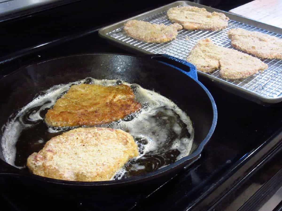 A cast iron skillet browning pork cutlets in oil.