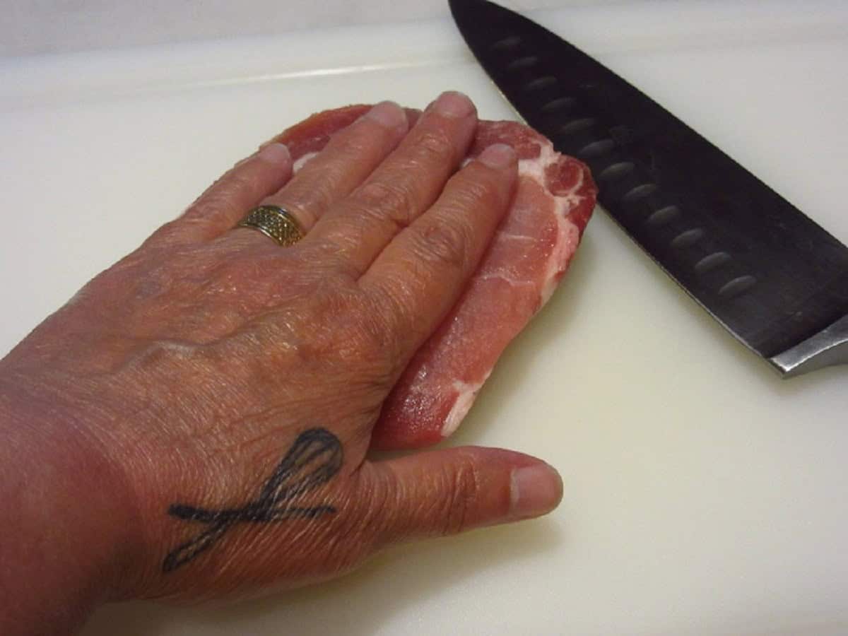 A knife, hand, and pork chop.
