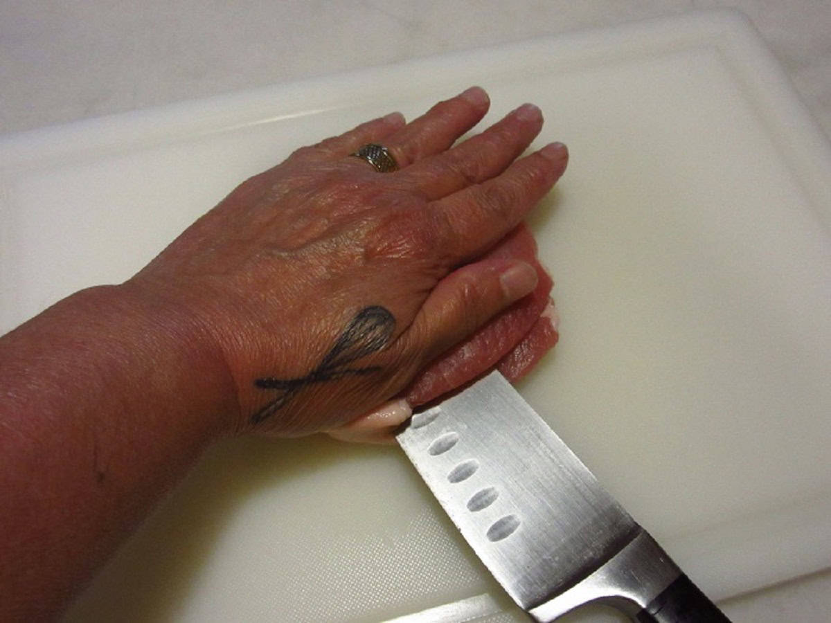 A hand helping guide a knife through a boneless pork chop.