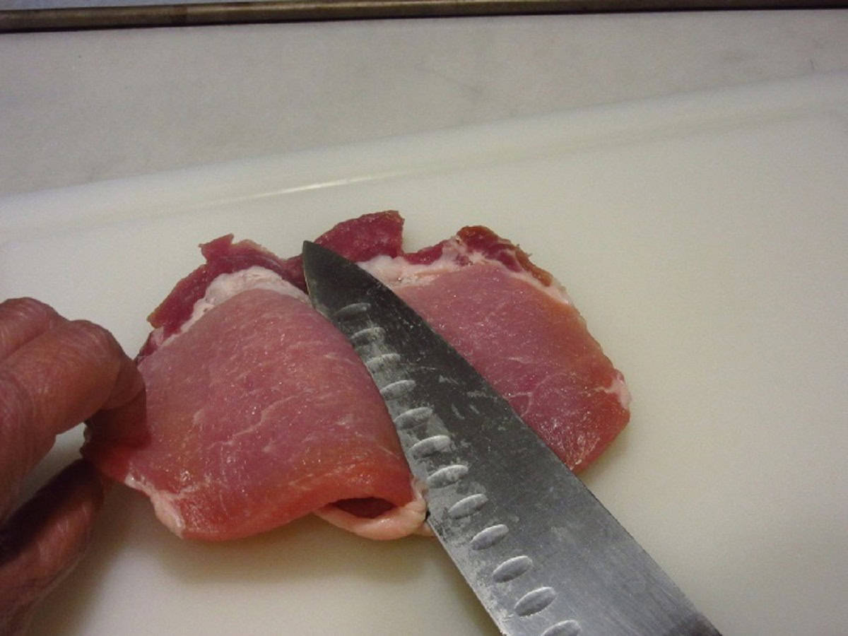 A knife trimming a pork chop in half.
