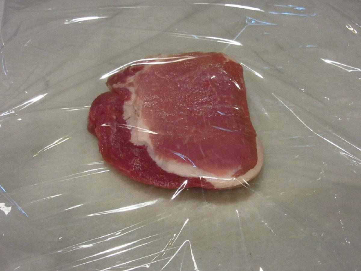 A boneless pork chop between plaststic wrap.