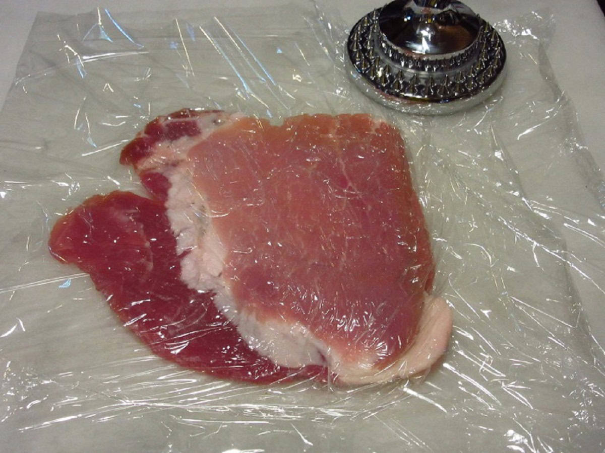 A pork cutlet between plastic wrap for pounding.