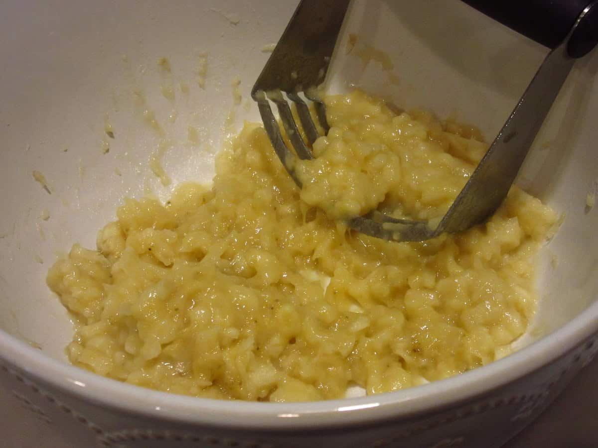 Mashed bananas in a white bowl with a pastry blender.