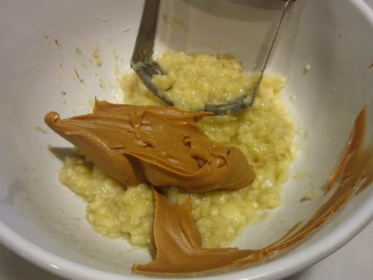 Peanut butter and mashed bananas in a white bowl with a pastry blender.