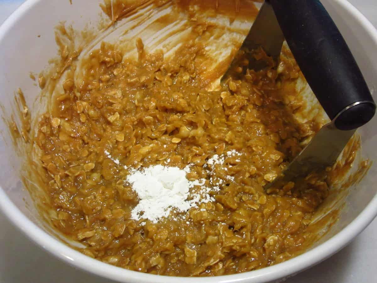 A pastry blender in a bowl of cookie dough with oatmeal.