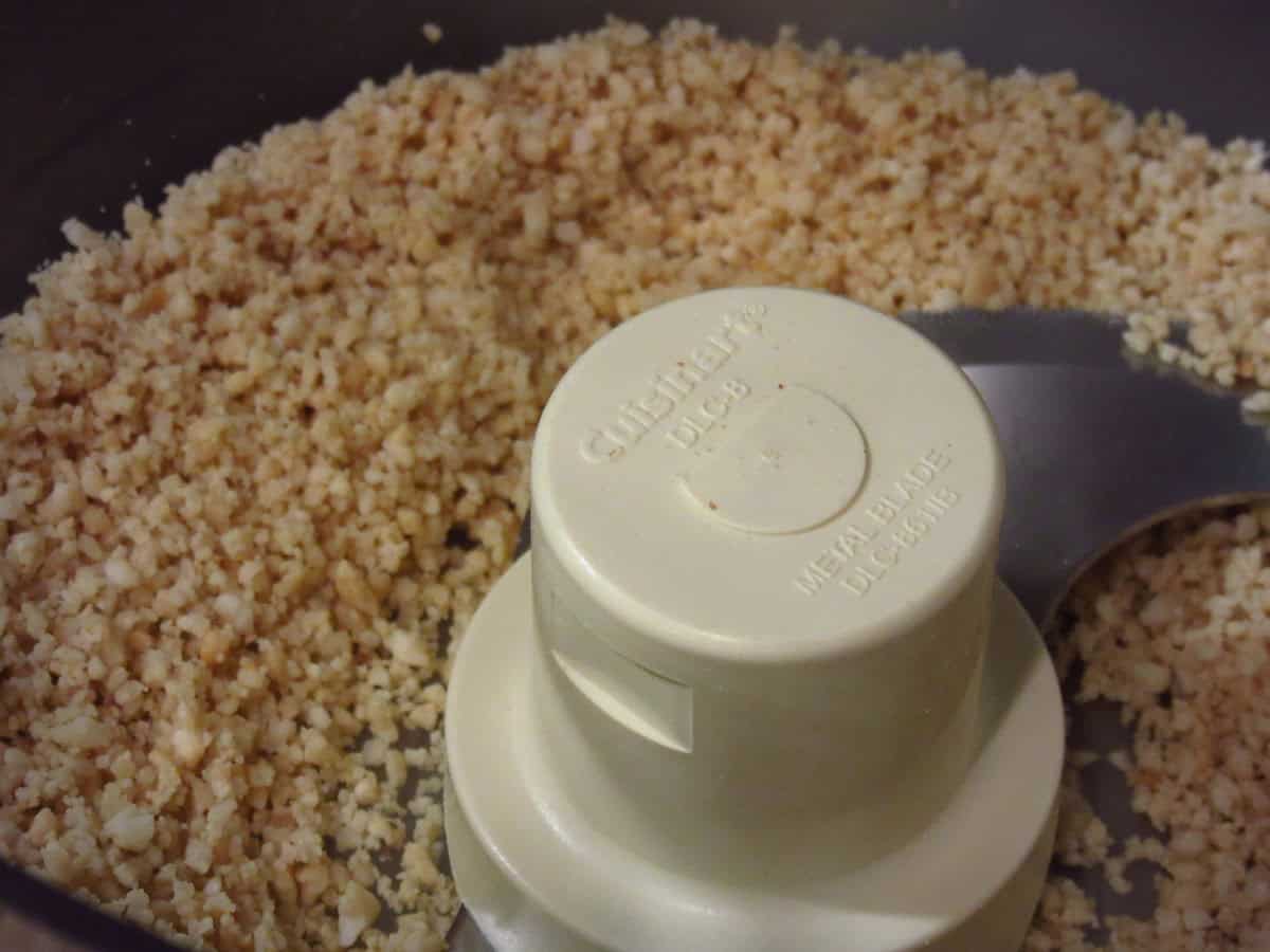 Chopped peanuts in the bowl of a food processor with the blade.