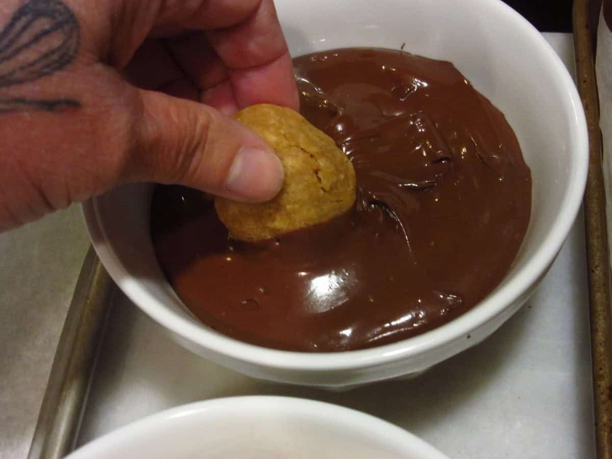 The top of a baked acorn cookie being dunked into melted chocolate.