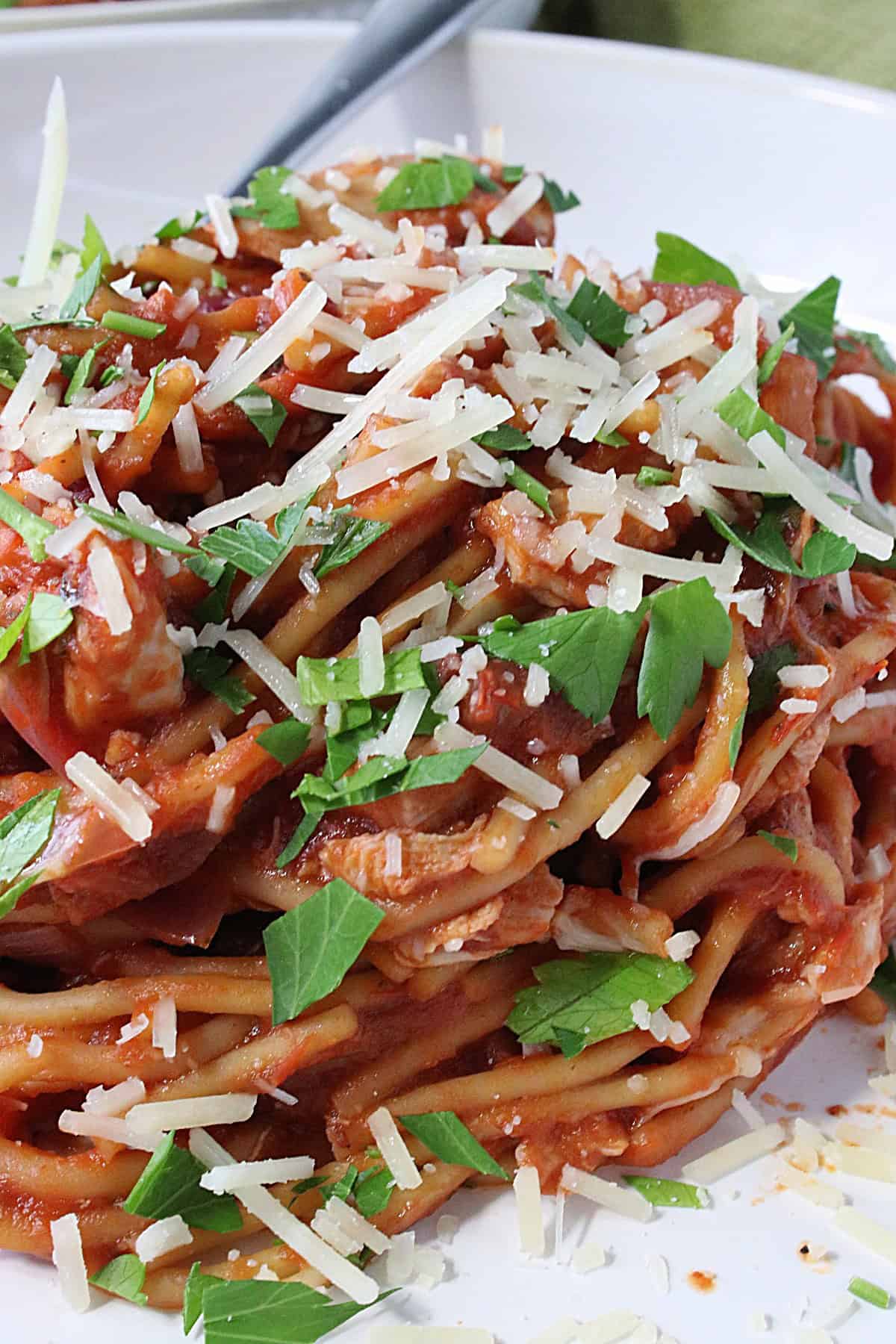 Chopped parsley on top of a pile of French Spaghetti in a white bowl.