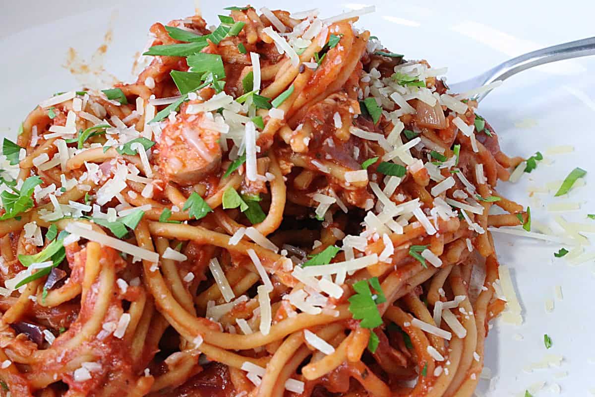 An inviting white bowl filled with French Spaghetti with Parmesan cheese, chicken, and parsley.