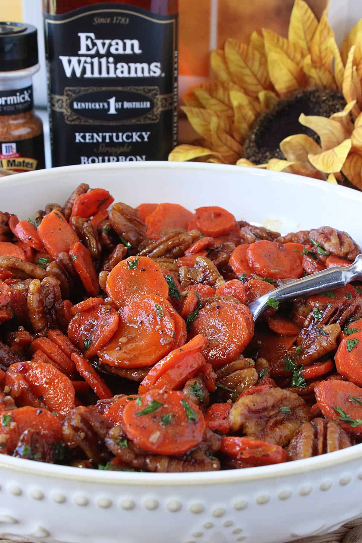 A bottle of Kentucky bourbon in the background of a bowl of cooked and glazed carrots in the foreground.