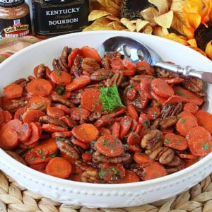 Pretty orange Kentucky Bourbon Glazed Carrots and Pecans in a white bowl with a spoon.