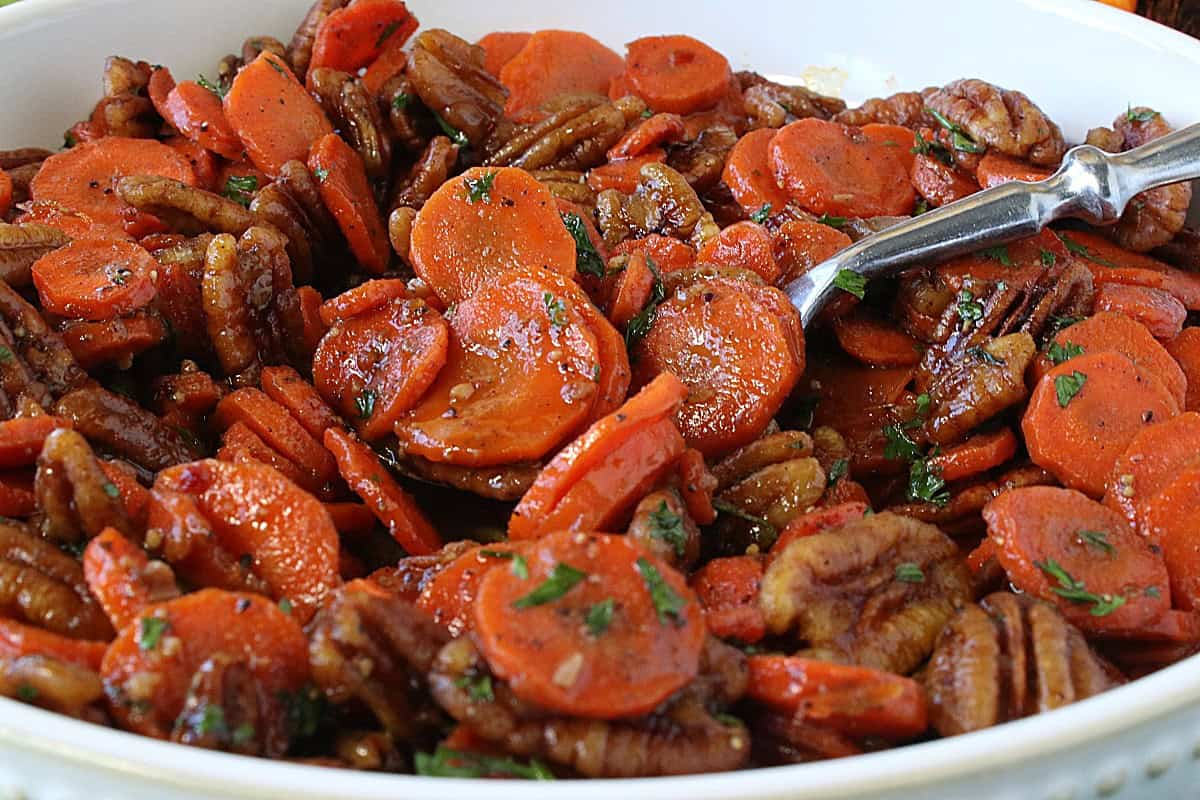 Beautiful cooked and glazed carrots in a bowl white bowl with a spoon.