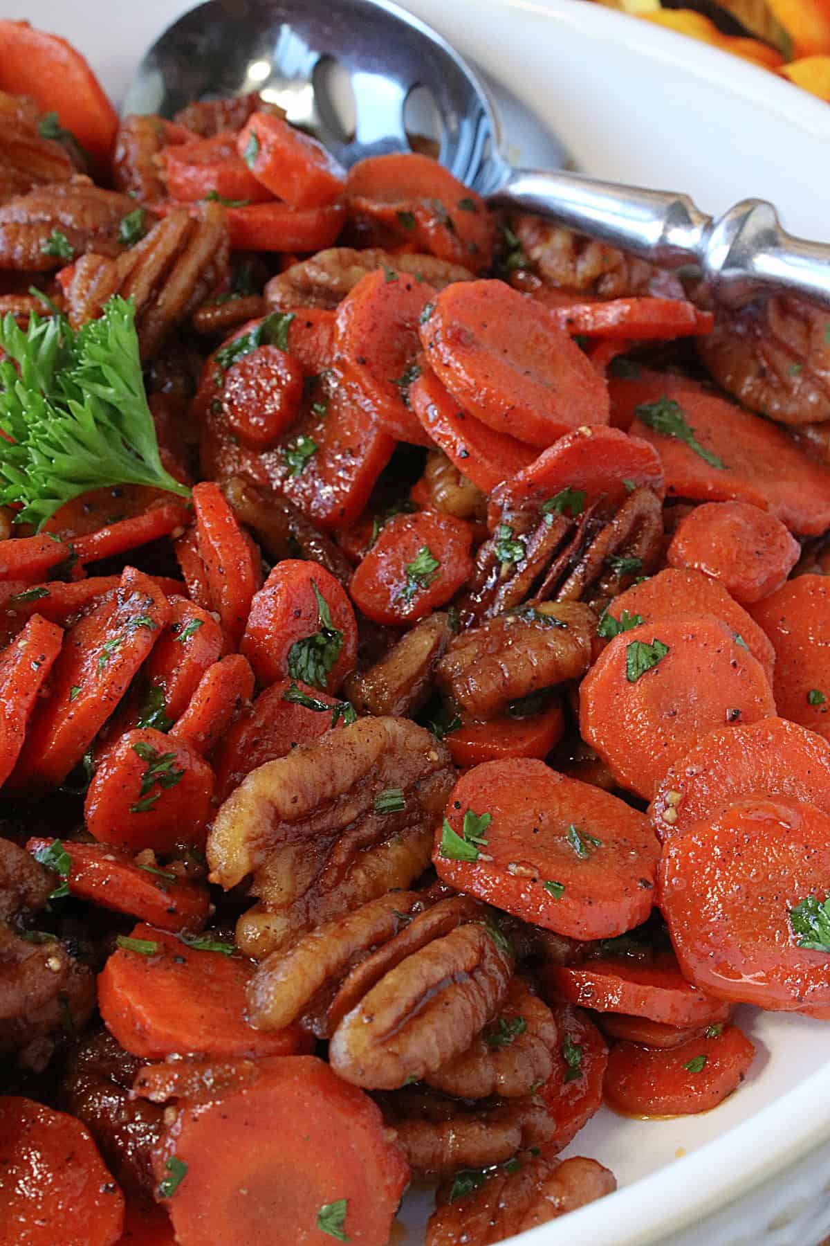 Orange cooked and glazed carrots and pecans topped with parsley in a white bowl