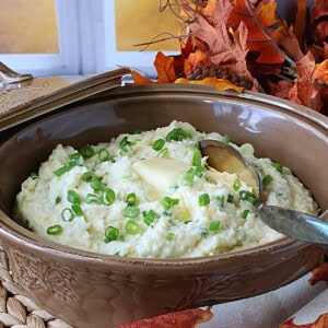 A tan casserole dish filled with Mashed Parsnips and Scallions along with melted butter and a spoon.