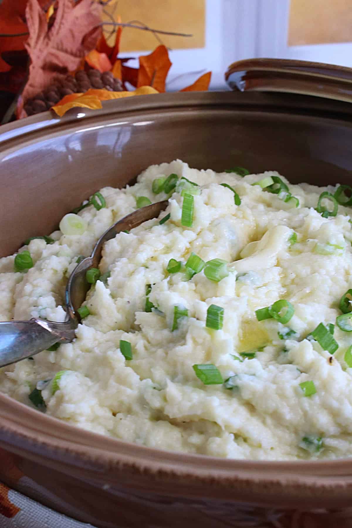 A serving spoon in a casserole dish filled with mashed parsnips and scallions.