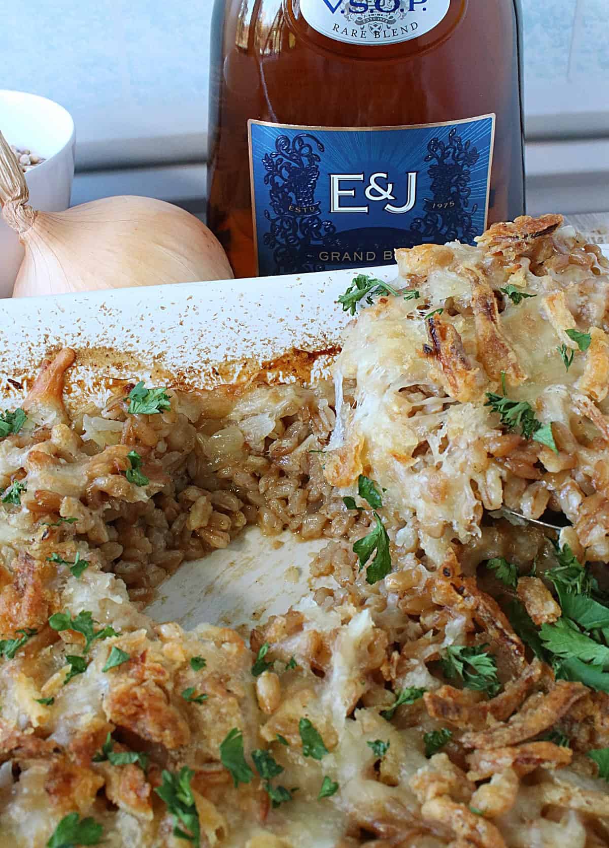 A white casserole dish with a spooned serving taken out of cheesy farro and onion casserole.