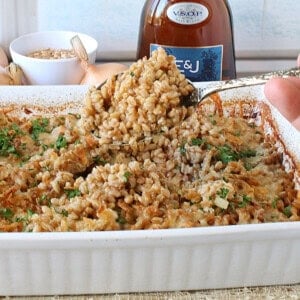 A hand holding a serving spoon filled with farro and onion casserole.