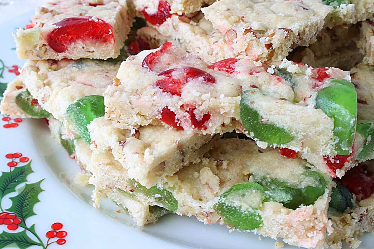 A closeup of a bar cookie with red and green cherries.