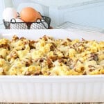 A white dish filled with a cheese top breakfast casserole with sausage and scrambled eggs.