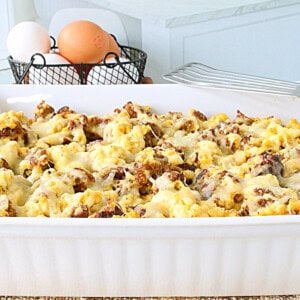 A white dish filled with a cheese top breakfast casserole with sausage and scrambled eggs.