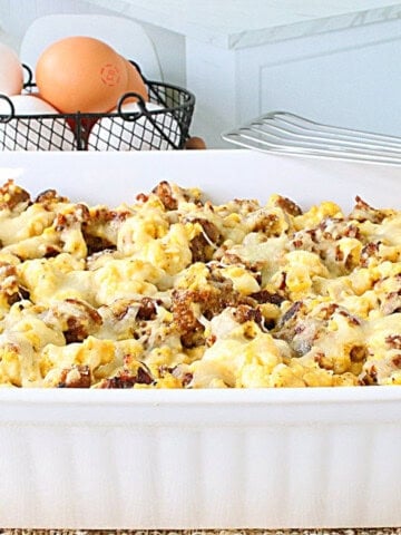 A white dish filled with a cheese top breakfast casserole with sausage and scrambled eggs.