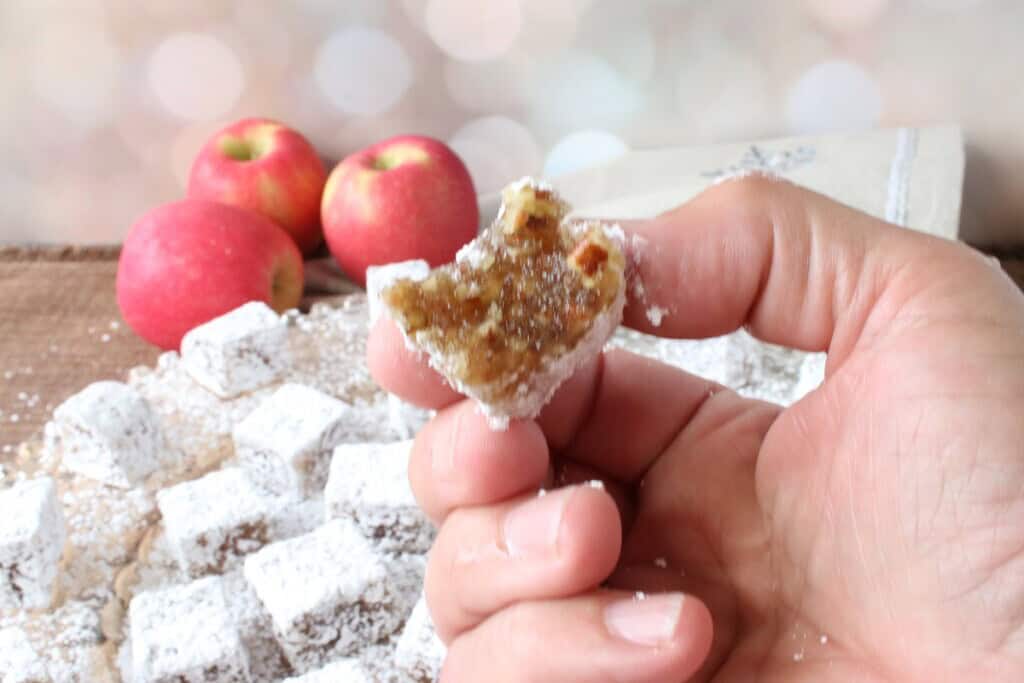 A hand holding an Old-Fashioned Apple Chews Candy with a bite taken out.